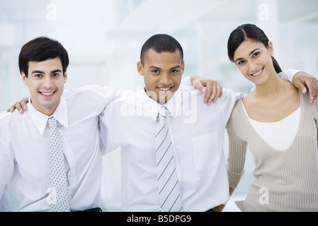 Three young professionals with arms around each other's shoulders, smiling at camera Stock Photo