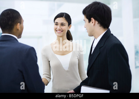 Professional woman standing with two businessman, shaking one man's hand, smiling Stock Photo