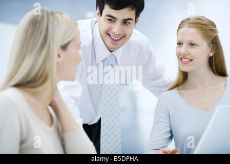 Businessman leaning over, chatting with female colleagues Stock Photo