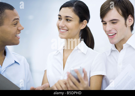 Young woman showing male colleagues her cell phone, smiling Stock Photo