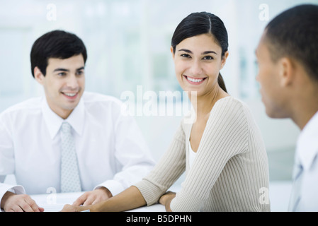 Young professional woman sitting with male colleagues, smiling at camera Stock Photo