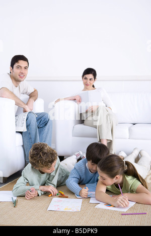 Family relaxing together in living room, children coloring on floor, father smiling at camera Stock Photo