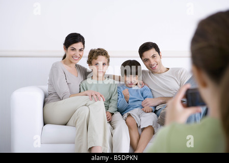 Family sitting on sofa, posing for photo being taken by daughter Stock Photo