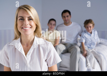 Portrait of smiling woman, family seated together on bed in background Stock Photo