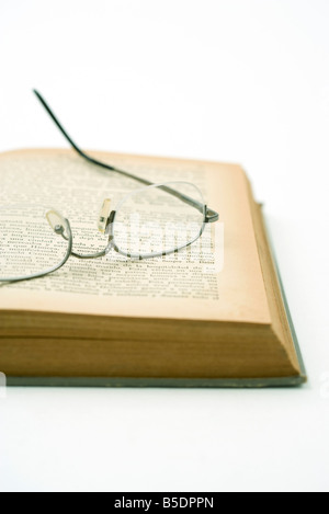 Pair of glasses resting on yellowed page of open book Stock Photo