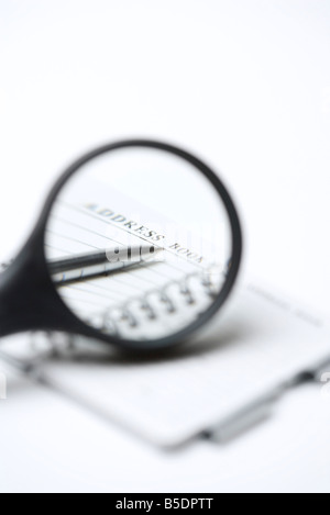 Magnifying glass over address book and pen, close-up Stock Photo