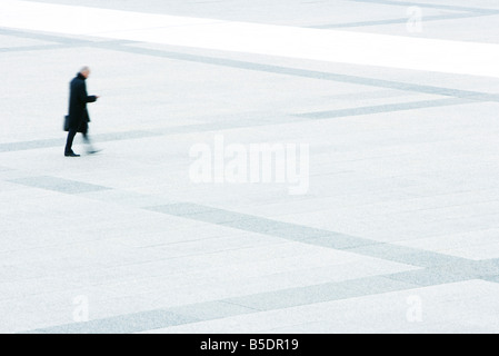 Businessman looking at his cell phone while walking across public square Stock Photo