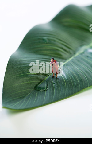 Miniature woman standing on leaf, water spilled in front of her Stock Photo
