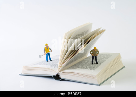 Miniature construction workers standing on open book Stock Photo