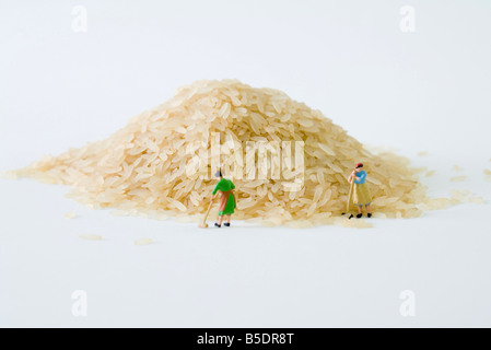 Miniature women sweeping large pile of rice Stock Photo