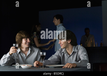 Friends having wine together at nightclub, smiling at each other, couple dancing in background Stock Photo