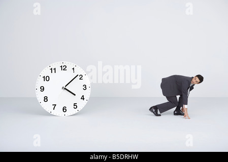 Businessman racing against time, looking over shoulder at large clock Stock Photo