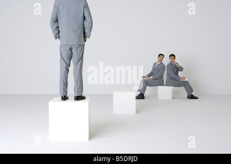 Two identical businessmen whispering over shoulders, third businessman watching Stock Photo