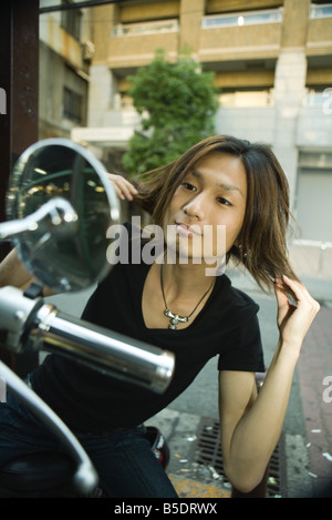 Young Japanese man seated on motorbike, fixing hair in side-view mirror Stock Photo
