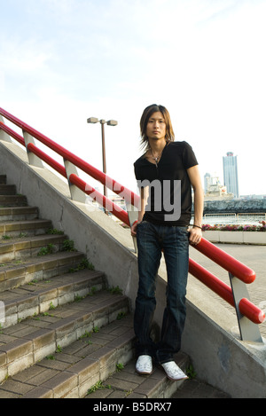 Young Japanese man standing on stairs, leaning against railing, portrait Stock Photo