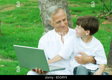 Boy sitting on grandfather's lap, using laptop computer Stock Photo