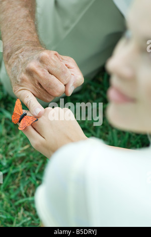 Butterfly landing on teenage girl's hand, man touching her hand with finger, over the shoulder view Stock Photo