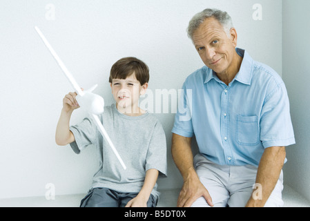 Grandfather sitting with grandson, smiling as grandson plays with toy airplane Stock Photo