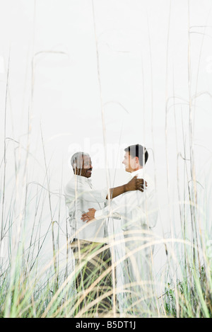 Two men facing each other in tall grass, smiling, embracing Stock Photo