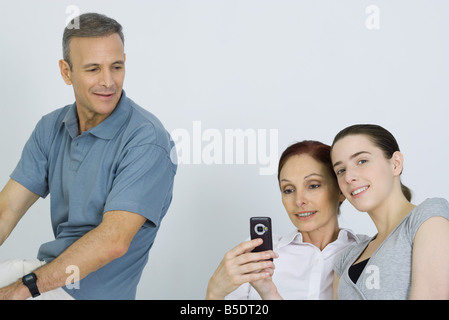 Family sitting together, parents looking at cell phone, daughter smiling at camera Stock Photo