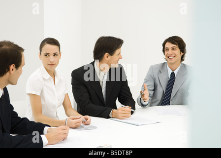 Business associates sitting around conference table, looking at each other, smiling Stock Photo