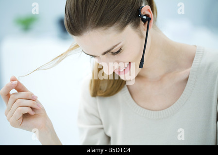 Young woman wearing headset, playing with hair and looking down, smiling Stock Photo