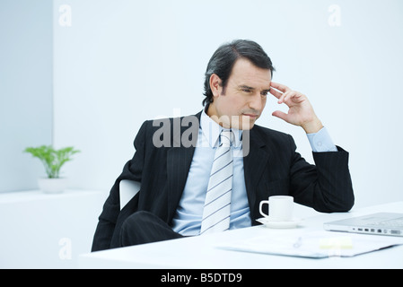 Businessman sitting at desk, holding head, looking away Stock Photo
