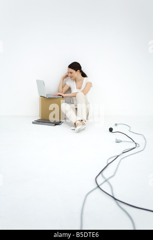 Young woman sitting on the ground, using laptop computer, loose electric cords nearby Stock Photo