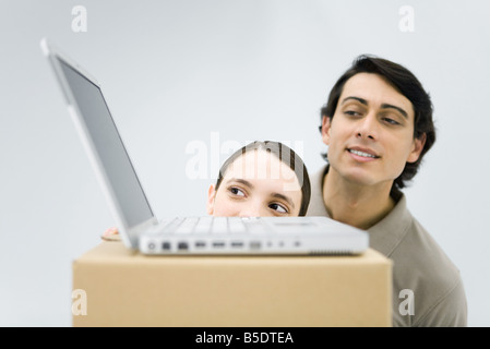 Man and woman peeking at laptop computer sitting on top of cardboard box Stock Photo