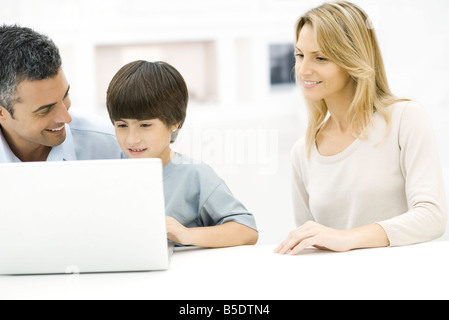Father and son using laptop computer together, mother watching Stock Photo