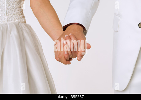 Bride and groom holding hands, mid section, close-up Stock Photo