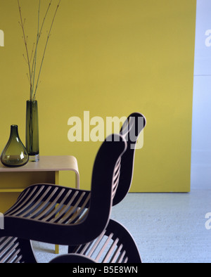 Slatted wooden chair and plywood table with modern glass vases in white dining room with bright yellow wall Stock Photo