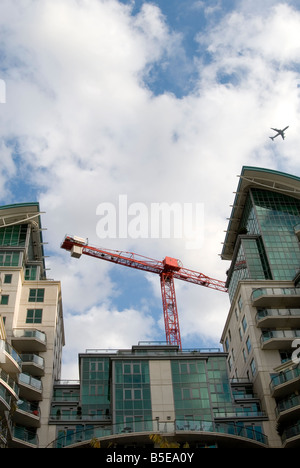 An image looking up at a modern block of london flats with a airplane flying above in the sky. A big red crane towers behind. Stock Photo