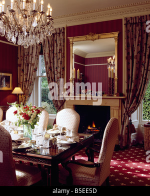 Glass chandelier above table set for lunch in dining room with patterned red carpet and gilt framed mirror above fireplace Stock Photo