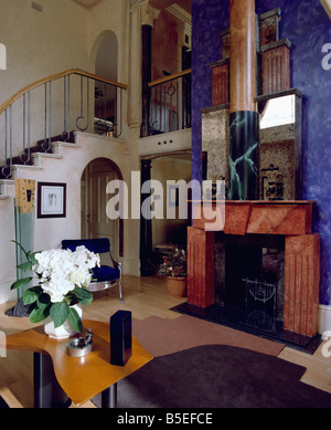 Painted marble-effect red fireplace on blue wall in eighties hall with fresh flowers on table Stock Photo