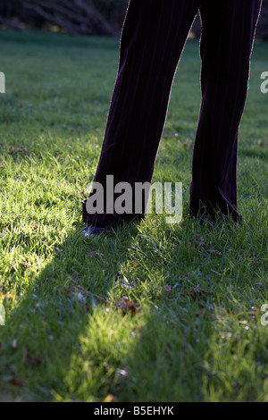 mans legs wearing suit in long grass with long shadow backlit Stock Photo