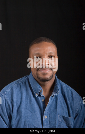 A black man posing in a denim shirt against a black background Stock Photo