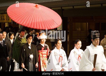A wedding procession at the Meiji Temple in Tokyo, Japan. The bride and groom walk under a red parasol. Stock Photo