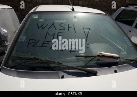 A Wash Me Please inscription plea written on the filthy windowscreen of a dirty car Stock Photo