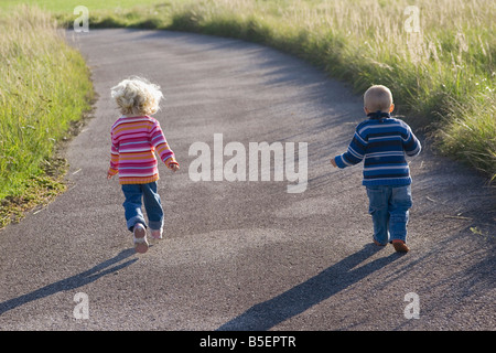 Little girl (2-3) and boy (1-2) running across path, rear view