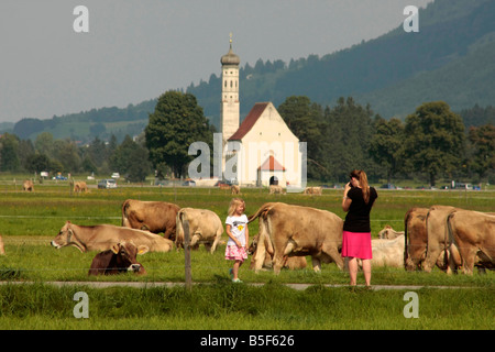 young girl posing with cows in front of St Coloman Church in Schwangau near Fuessen Allgaeu Bavaria Germany Stock Photo