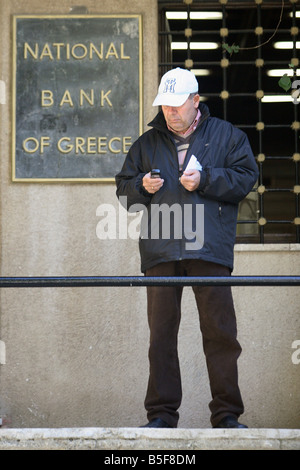 Man in front of a branch of the National Bank of Greece in Rhodes, Greece Stock Photo