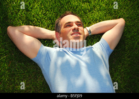 A man lying on green grass relaxing Stock Photo