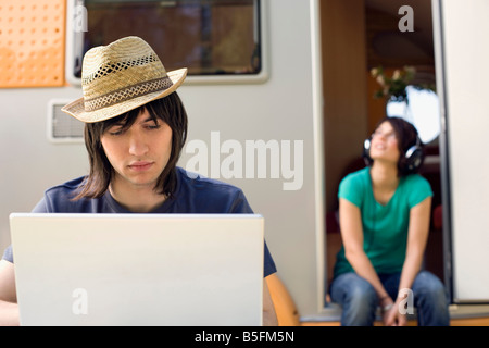 Germany, Leipzig, Ammelshainer See, Young couple, man using laptop, woman listening to headphones Stock Photo