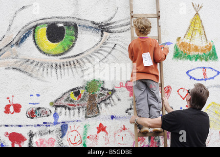 Boy standing on a ladder and painting on a wall Stock Photo