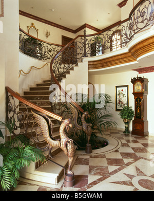 Ornate wrought-iron bannisteers on curved staircase in Spanish hall with brown & white marble floor tiles Stock Photo
