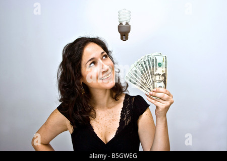 Woman waving money and looking up Having an environmentally friendly idea with an energy saving fluorescent light bulb floating Stock Photo