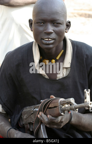 A young Dinka man in a cattle camp near Rumbek, South Sudan keeps his AK-47 close. Stock Photo