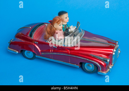 Pressed metal novelty toy battery powered car with driver sitting beside a woman photographer with camera and flash. Stock Photo