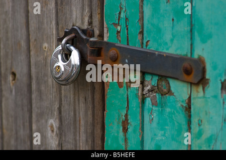 Locked and rusted padlock on green and grey wooden shed door Stock Photo
